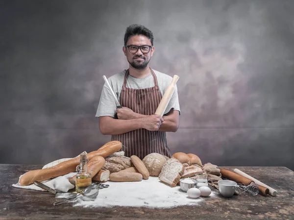 Asian man posing with bread and cooking staff at table in bakery.