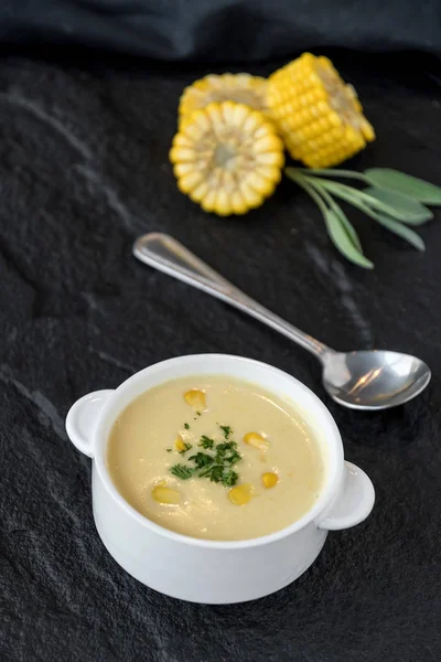 Top view of corn soup in bowl with fresh corn cob on black stone plate.