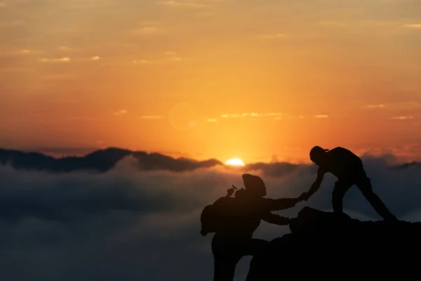 Two friends helping each other trying to reach top of mountains during wonderful summer sunset.