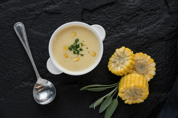 Top view of corn soup in bowl with fresh corn cob on black stone plate.