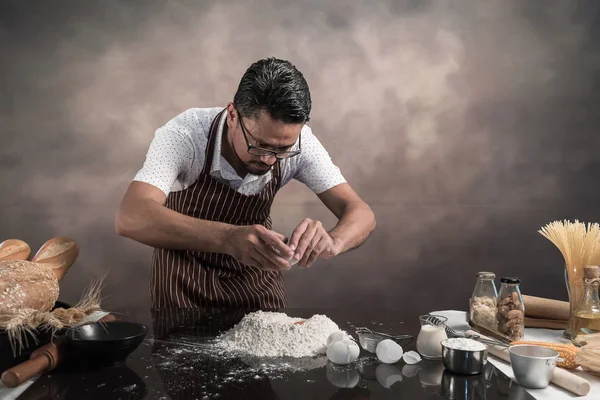 Man preparing buns at table in bakery. Man sprinkling flour over fresh dough on kitchen table.