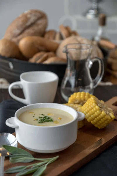 Corn soup in bowl with fresh corn cob on wooden board.