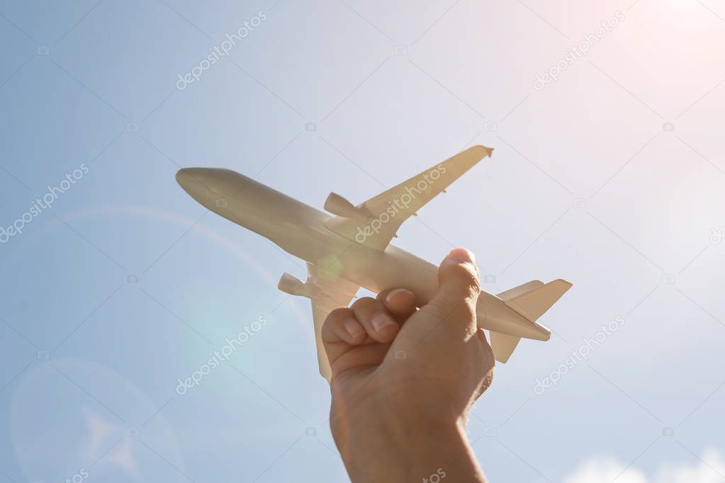 Airplane model in human hand on sky background with sunshine.