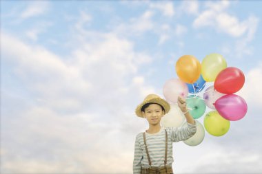 Grup mavi bulutlu gökyüzü arka plan üzerinde renkli balonlar ile mutlu Asyalı çocuk.