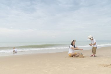 İki sevimli oğlu ile kumsalda oynarken annesi.