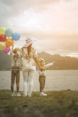 Asyalı kadının oğulları balonlar ile sahilde birlikte ayakta arkadan görünüş.