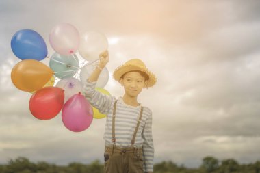 Asyalı çocuk renkli balonlarla kumsalda oynarken fotoğrafını tonda.