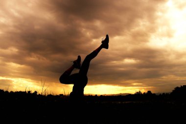 Pratik Yoga sahilde günbatımı zaman alacakaranlık gökyüzü arka plan ile Lady karanlık siluet