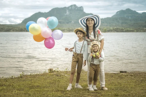 Asyalı kadın balonlar ile plajda durup oğulları sarılma.