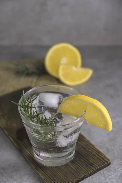 Alcoholic drink gin tonic with lemon, rosemary and ice on table.