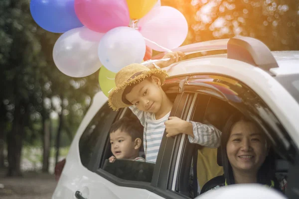 Happy family holding colorful balloons in car having great holiday on summer.