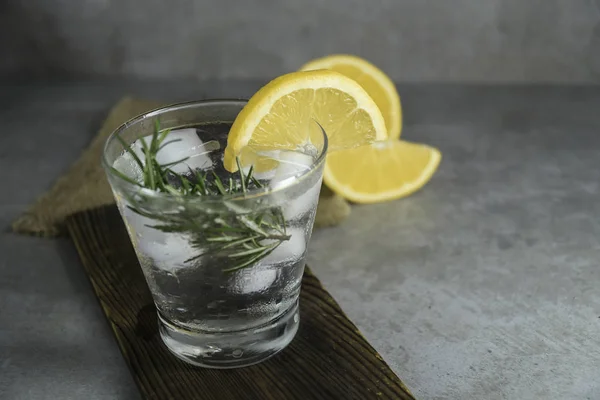 Alcoholic drink gin tonic with lemon, rosemary and ice on table.