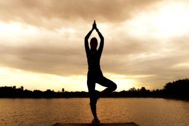 Pratik Yoga sahilde günbatımı zaman alacakaranlık gökyüzü arka plan ile kadın silüeti