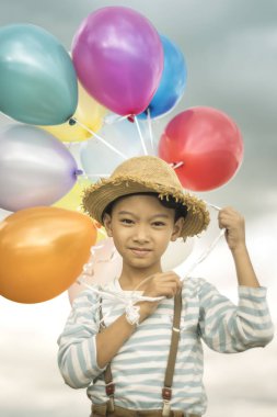 Asyalı çocuk renkli balonlarla kumsalda oynarken portresi.