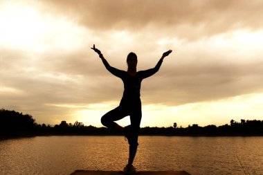 Pratik Yoga sahilde günbatımı zaman alacakaranlık gökyüzü arka plan ile kadın silüeti