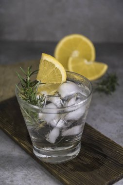 Alkollü içki cin tonik limon, biberiye ve buz gri arka plan üzerinde ahşap tahta üzerinde.