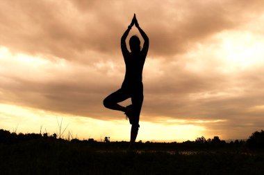 Kadın siluet pratik yoga sahilde günbatımı zaman alacakaranlık gökyüzü arka plan ile