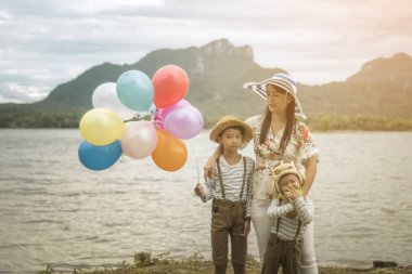 Asyalı kadın balonlar ile plajda durup oğulları sarılma.