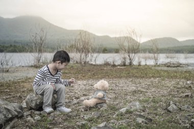 Sevimli küçük Asya çocuk taşları, Tayland üzerine oturan bir oyuncak ayı ile.
