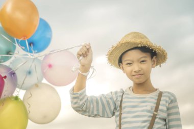 Asyalı çocuk renkli balonlarla kumsalda oynarken portresi.