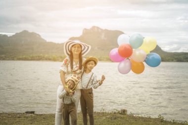Asyalı kadın balonlar ile plajda durup oğulları sarılma.