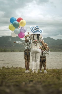 Asyalı kadının oğulları balonlar ile plajda durup sarılma arkadan görünüş.