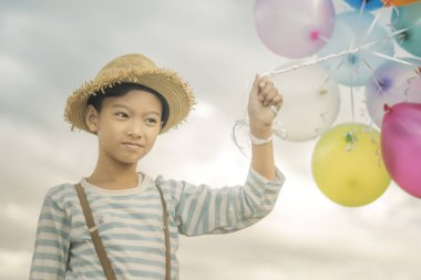 Asyalı çocuk renkli balonlarla kumsalda oynarken portresi.