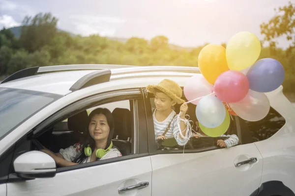 Happy family holding colorful balloons outdoor in car having great holidays time.