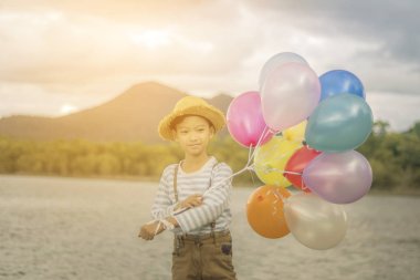 Renkli balonlar riverside adlı tutan mutlu Asyalı çocuk.