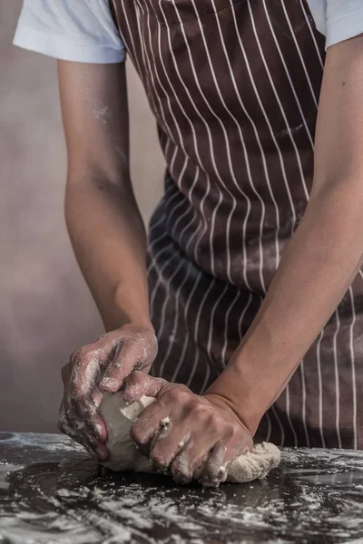 Man preparing buns at table in bakery, Man sprinkling flour over fresh dough on kitchen table