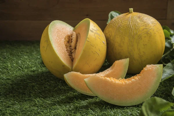 Cut and whole melons on green background.