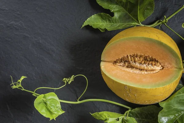 Cut melon with green leaves on background with copy space.