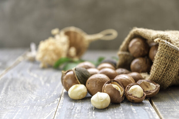 Macadamia nuts scattered from sack on wooden background.