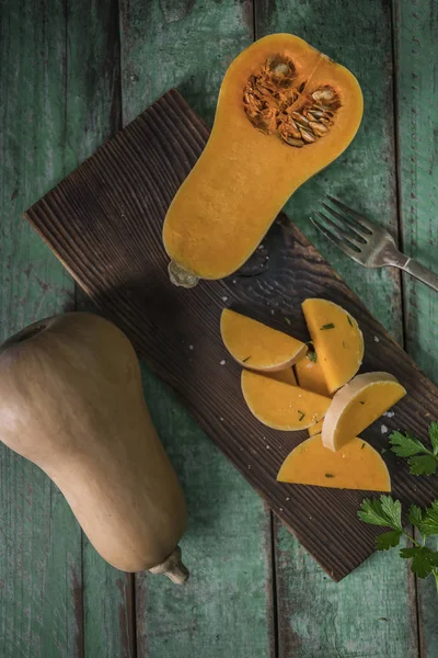 Sliced butternut squashes over old wood background, Pumpkin pieces, harvest, fall. Dark brown background. Cooking in autumn. Healthy food.