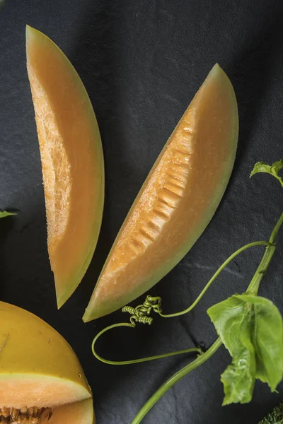 Cut melon with green leaves on background with copy space.