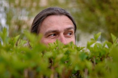 Sakallı ve bıyıklı bir adam çalılıkların arkasından parkta gözetleniyor..