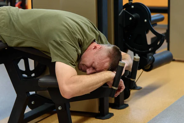 Tired man in the gym behind a fitness station.