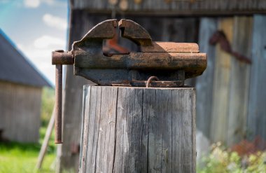 Eski paslı mengene. Köyün arka bahçesinde bir kütük üzerinde duran