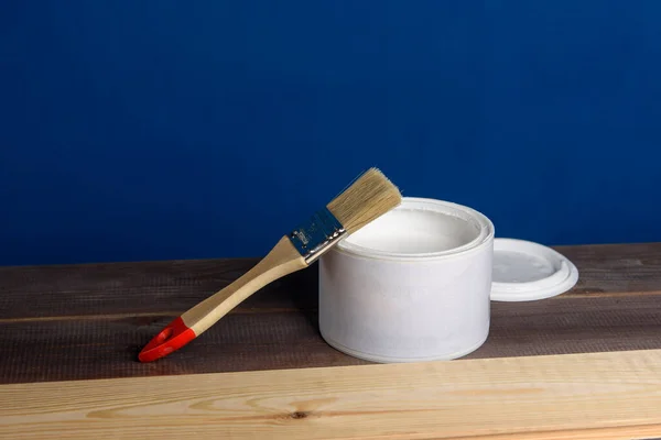 Tahtayı beyaz boyayla boyuyorum. Bir kutu boya ve ahşap masada bir fırça..