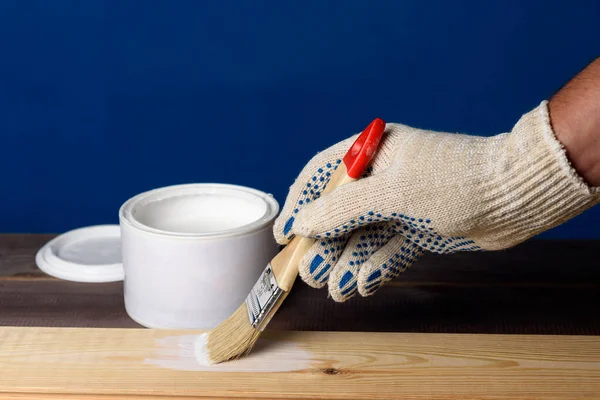 Tahtayı beyaz boyayla boyuyorum. Bir kutu boya ve ahşap masada bir fırça..
