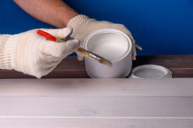 Tahtayı beyaz boyayla boyuyorum. Bir kutu boya ve ahşap masada bir fırça..