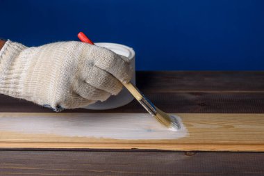 Tahtayı beyaz boyayla boyuyorum. Bir kutu boya ve ahşap masada bir fırça..