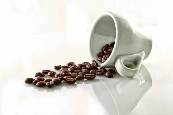 白い背景の上にコーヒー カップから落ちてくるいくつかのコーヒー豆 — ストック写真