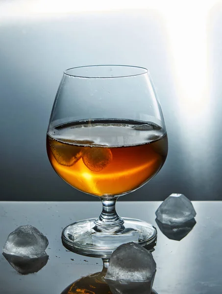 Whiskey, bourbon, brandy or cognac with ice on a blue background.