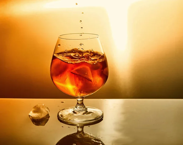 オレンジ色の背景に滴と氷とウイスキーのガラス ウイスキーのガラスとドロップシンボルデザイン — ストック写真
