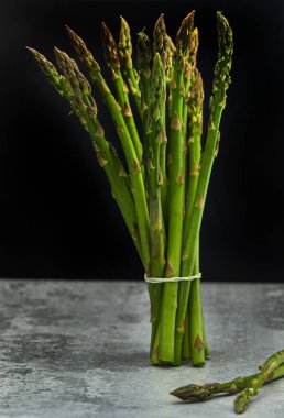 Beton taban ve siyah bir arka plan üzerinde taze kuşkonmaz Demet.