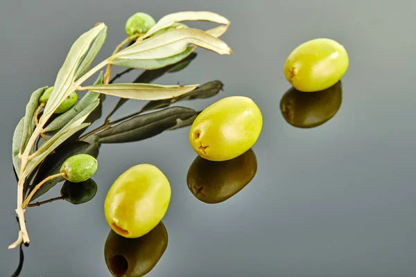 Three olives with olive tree branch with fruits lying on a gray background — Stock Photo, Image