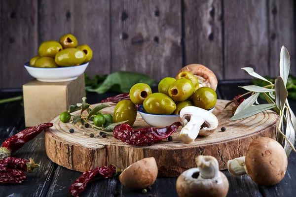 Still life of green fresh olives, red pepper and fresh mushrooms with olive tree leaves on a dark wooden Royalty Free Stock Images