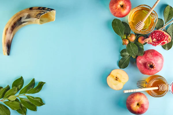 Rosh hashanah - Yahudi Yeni Yıl tatili konsepti. Geleneksel semboller: Bal kavanozu ve narlı taze elmalar ve mavi arka planda shofar boynuzu. Metin için alanı kopyala.