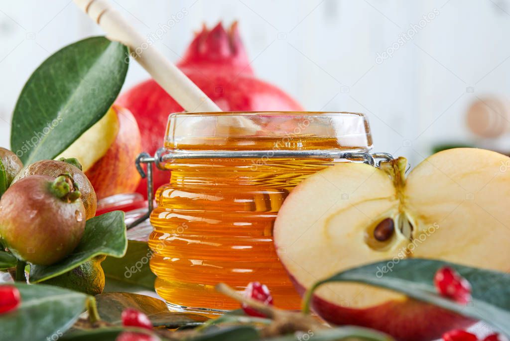Rosh hashanah - jewish New Year holiday concept. Traditional symbols: Honey jar and fresh apples with pomegranate on white wooden background. Copy space